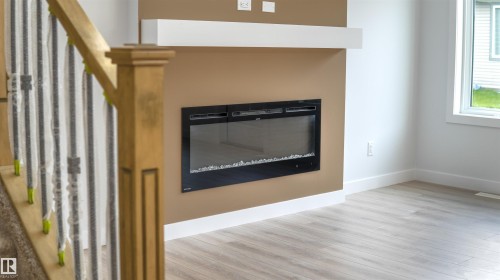 Integrated electric fireplace with a white mantel, light wood-finish flooring, and white baseboards - 3708 40 Ave, Beaumont, AB 