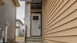 Entryway featuring a white paneled door with window, stone accent column, concrete steps, and a dark wood handrail - 