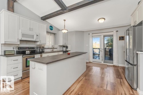 Modern kitchen featuring wood-finish flooring, white cabinetry, stainless steel appliances, a center island, and a vaulted ceiling with exposed beams - 1112 13 Avenue, Cold Lake, AB - Indoor Photo Showing Kitchen