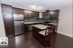 Kitchen with dark wood cabinetry, stainless steel appliances, light granite countertops, a dark tile backsplash, and dark wood-finish flooring - 