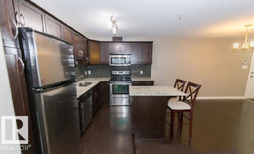 Open-concept kitchen featuring dark wood cabinetry, stainless steel appliances, granite countertops, and a subway tile backsplash - #141 11505 Ellerslie Rd, Edmonton, AB 