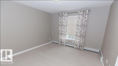 Room featuring light neutral-toned walls, beige carpeting, and white baseboards - #141 11505 Ellerslie Rd, Edmonton, AB 