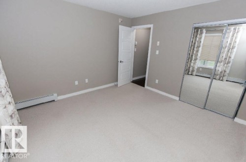 Carpeted room featuring a mirrored sliding closet door, neutral wall paint, white trim, and a white interior door - #141 11505 Ellerslie Rd, Edmonton, AB 