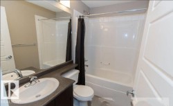 Bathroom with a white toilet, integrated bathtub and shower, and a vanity featuring a single basin sink and dark wood-finish cabinetry - 