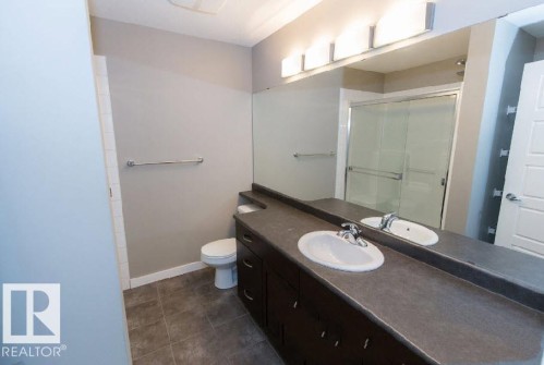 Bathroom featuring a dark wood-finish vanity with an integrated sink, a large wall-mounted mirror, and a shower with a sliding glass door - #141 11505 Ellerslie Rd, Edmonton, AB 