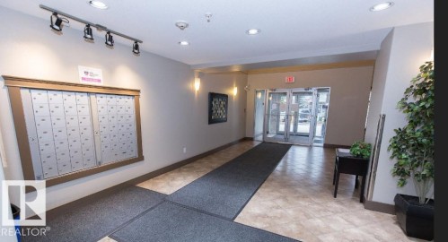 Building entryway featuring multi-pane glass doors, recessed lighting, track lighting, wall-mounted mailboxes, and patterned floor tiles - #141 11505 Ellerslie Rd, Edmonton, AB 