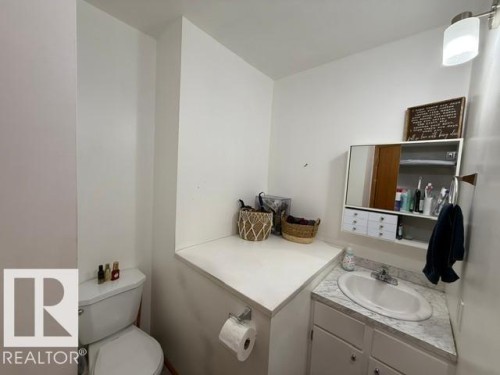 Compact bathroom featuring a white porcelain toilet, a corner vanity with a built-in sink, and a mirrored medicine cabinet - 4917 45 Avenue, Vegreville, AB - Indoor Photo Showing Bathroom