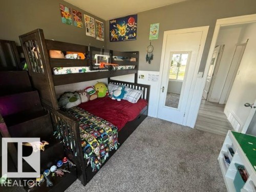 Bedroom featuring a dark wood-finish bunk bed with integrated storage steps, light gray wall paint, and a plush gray carpet - 4917 45 Avenue, Vegreville, AB - Indoor Photo Showing Bedroom