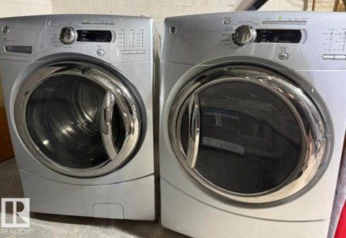 Front-loading washer and dryer set featuring metallic silver finishes, chrome door accents, digital display, and rotary controls - 4917 45 Avenue, Vegreville, AB - Indoor Photo Showing Laundry Room