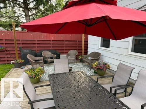 Expansive exterior wooden deck featuring a red privacy fence, white siding, and two windows - 4917 45 Avenue, Vegreville, AB - Outdoor With Deck Patio Veranda With Exterior