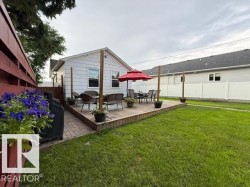 Rear exterior featuring an elevated wood deck, a patio area with paver stones, white vinyl siding, and a manicured lawn - 