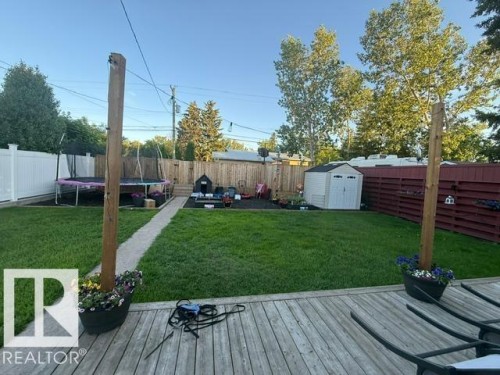 Expansive backyard featuring a wood deck, manicured lawn, and a white storage shed - 4917 45 Avenue, Vegreville, AB - Outdoor With Deck Patio Veranda