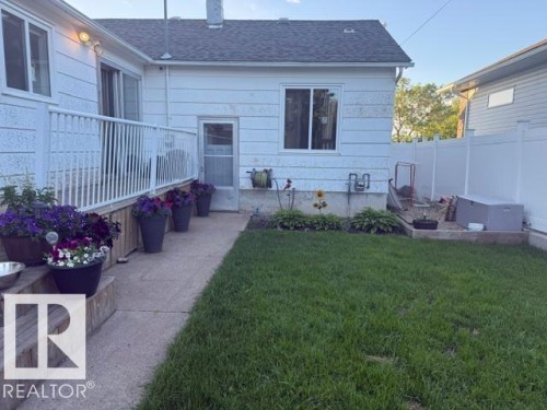Manicured lawn area featuring a concrete pathway, white vinyl fencing, a raised garden bed, and exterior siding - 4917 45 Avenue, Vegreville, AB - Outdoor With Exterior