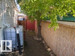 Siding exterior featuring a rain barrel system, a natural reed privacy screen, and a wooden gate with red lattice - 