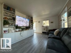 Spacious living area featuring wood-finish flooring, a full-wall built-in media center with open shelving and closed cabinetry, and a shiplap accent wall - 