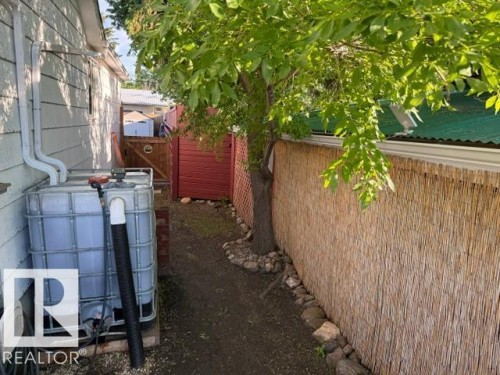 Siding exterior featuring a rain barrel system, a natural reed privacy screen, and a wooden gate with red lattice - 4917 45 Avenue, Vegreville, AB - Outdoor