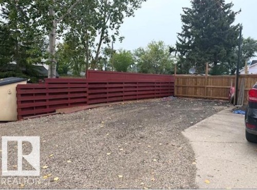 Gravel lot with partial concrete surfacing and a tall red-painted wooden privacy fence - 4917 45 Avenue, Vegreville, AB - Outdoor