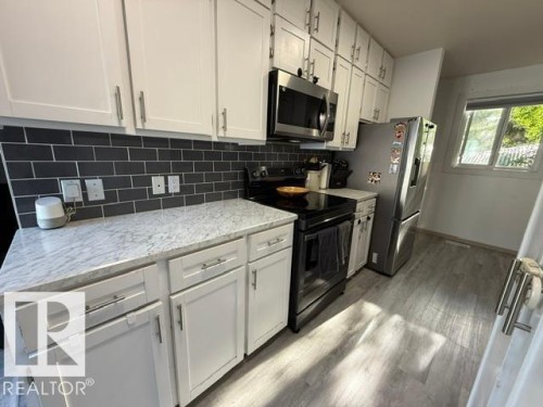 Modern kitchen featuring white shaker cabinetry, a dark subway tile backsplash, and light-toned countertops - 4917 45 Avenue, Vegreville, AB - Indoor Photo Showing Kitchen