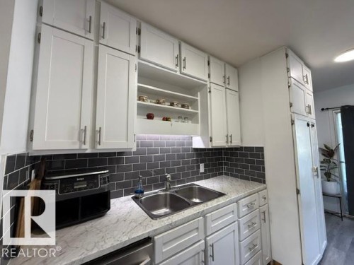 White shaker-style cabinetry with brushed nickel hardware, a double-basin stainless steel sink, and light-toned, veined countertops - 4917 45 Avenue, Vegreville, AB - Indoor Photo Showing Kitchen With Double Sink