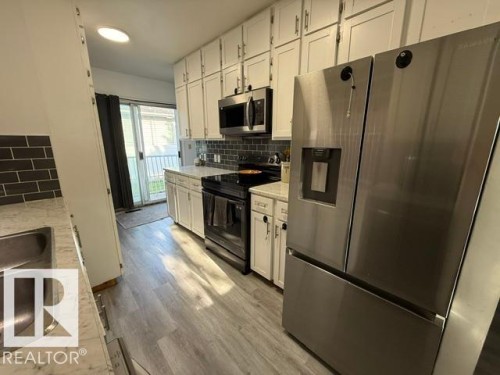 Contemporary kitchen featuring stainless steel appliances, white cabinetry, a black subway tile backsplash, and light wood-finish flooring - 4917 45 Avenue, Vegreville, AB - Indoor Photo Showing Kitchen