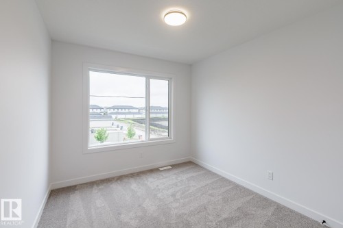 Bright room featuring a large window, neutral gray carpeting, white walls, white trim, and a flush-mount ceiling light fixture - 6308 65 Avenue, Beaumont, AB 