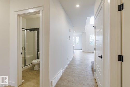 Bright hallway with wood-finish flooring, leading to a bathroom featuring a glass-enclosed shower with a built-in bench and dark tile surround - 6308 65 Avenue, Beaumont, AB 
