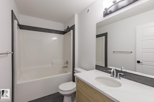 Bathroom featuring a spacious white tub/shower combination, dark gray tile surround, light wood-finish vanity, white countertop with an integrated sink, and a large wall-mounted mirror - 6308 65 Avenue, Beaumont, AB 