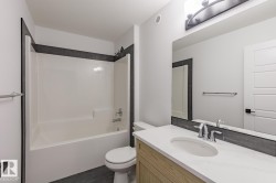 Bathroom featuring a spacious white tub/shower combination, dark gray tile surround, light wood-finish vanity, white countertop with an integrated sink, and a large wall-mounted mirror - 