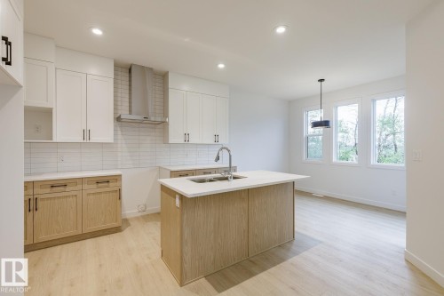 Contemporary kitchen featuring two-tone cabinetry with light wood-finish lower cabinets and white upper cabinets, white subway tile backsplash, and light wood-finish flooring - 6308 65 Avenue, Beaumont, AB 