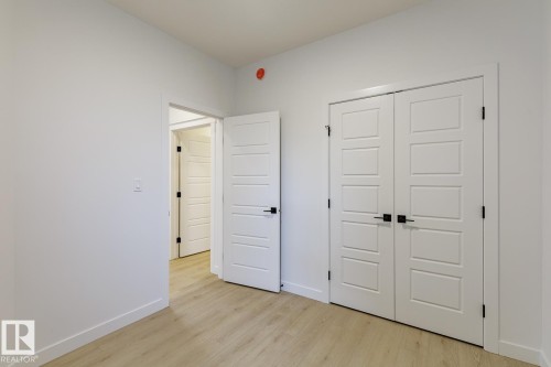 Room featuring light wood-finish flooring, white walls, and a pair of white paneled doors with black hardware - 6308 65 Avenue, Beaumont, AB 