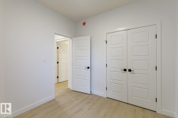 Room featuring light wood-finish flooring, white walls, and a pair of white paneled doors with black hardware - 