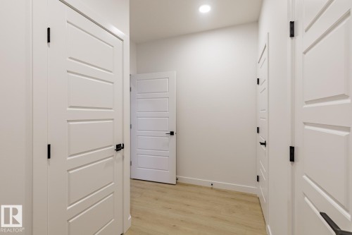Interior hallway featuring light wood-finish flooring, recessed lighting, and multiple white doors with modern black hardware - 6308 65 Avenue, Beaumont, AB 
