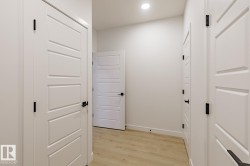 Interior hallway featuring light wood-finish flooring, recessed lighting, and multiple white doors with modern black hardware - 