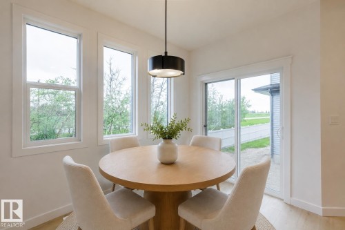 Dining area featuring a circular wood-finish table, three vertical windows with white trim, a sliding glass door, and recessed lighting - 6308 65 Avenue, Beaumont, AB 