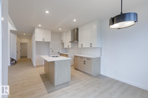 Contemporary kitchen featuring an island with a sink and a quartz countertop, white shaker cabinetry, stainless steel appliances, subway tile backsplash, and light wood-finish flooring - 6308 65 Avenue, Beaumont, AB 