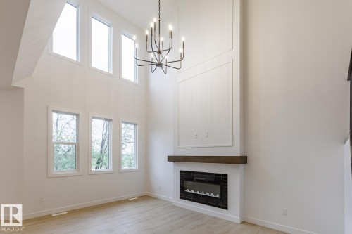 Two-story living area with wood-finish flooring, a contemporary black metal chandelier, and multiple large windows - 6308 65 Avenue, Beaumont, AB 