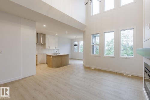 Spacious open-concept living area featuring high ceilings, light wood-finish flooring, and expansive windows - 6308 65 Avenue, Beaumont, AB 