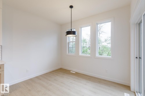 Bright interior space featuring a contemporary black pendant light, three large windows with white trim, wood-finish flooring, and a sliding glass door - 6308 65 Avenue, Beaumont, AB 