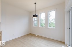 Bright interior space featuring a contemporary black pendant light, three large windows with white trim, wood-finish flooring, and a sliding glass door - 
