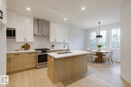 Modern kitchen featuring two-tone cabinetry, stainless steel appliances, a subway tile backsplash, and a central island with a sink - 6308 65 Avenue, Beaumont, AB 