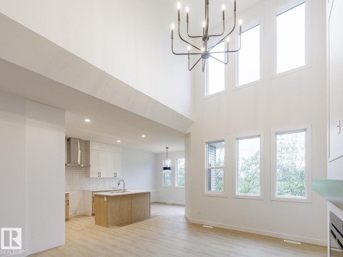 Two-story ceiling height with a contemporary chandelier, multiple windows, light wood-finish flooring, and a kitchen featuring a wood-finish island with a sink - 6308 65 Avenue, Beaumont, AB 