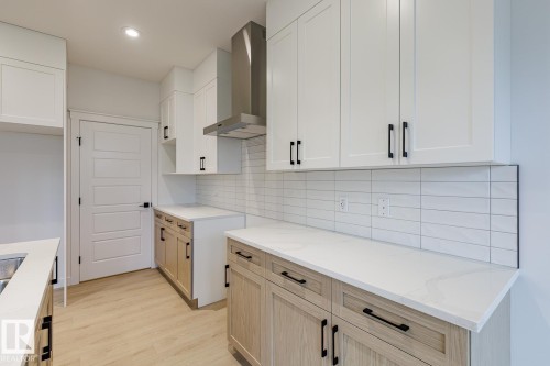 Contemporary kitchen featuring white shaker upper cabinetry and wood-finish lower cabinetry, complemented by white countertops and a subway tile backsplash - 6308 65 Avenue, Beaumont, AB 