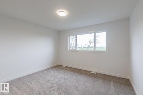 Neutral-toned room featuring a large window, light-colored walls, and gray carpet flooring - 6308 65 Avenue, Beaumont, AB 