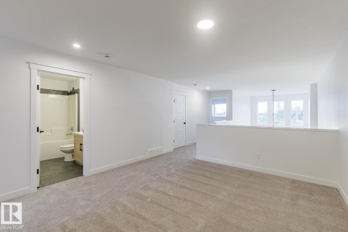 Spacious carpeted room featuring a full bathroom with a tub/shower combination, dark tile flooring, and a light-colored vanity - 6308 65 Avenue, Beaumont, AB 