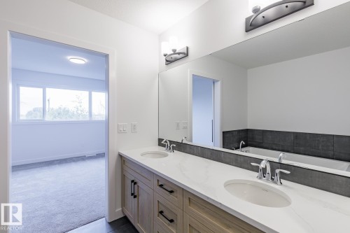 Double vanity with a white countertop and undermount sinks, featuring chrome faucets and modern wall-mounted light fixtures - 6308 65 Avenue, Beaumont, AB 
