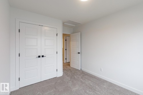 Bedroom featuring light gray carpeting, white walls, white trim, and a white paneled door with black hardware - 6308 65 Avenue, Beaumont, AB 