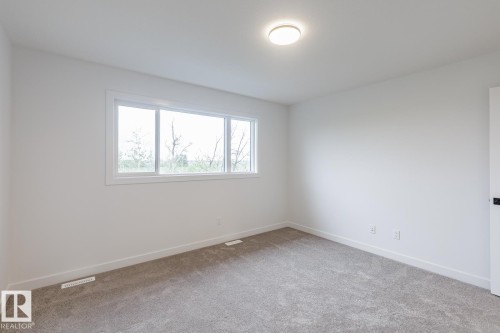 Bright interior space featuring a large window, neutral wall paint, and gray carpeting - 6308 65 Avenue, Beaumont, AB 