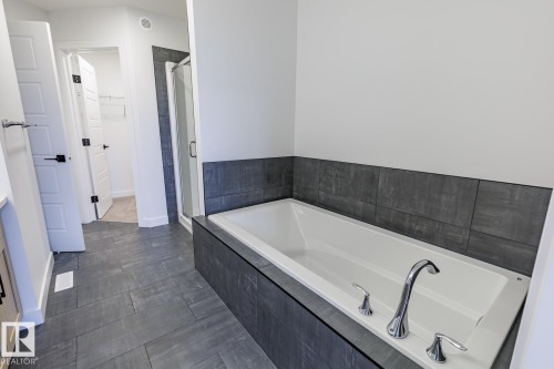 Built-in soaking tub with chrome fixtures, surrounded by dark-toned tile - 6308 65 Avenue, Beaumont, AB 