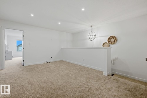Carpeted loft area featuring a modern orb chandelier, recessed lighting, white half-wall railing, and a doorway to an additional room - 22924 82 Ave, Edmonton, AB 