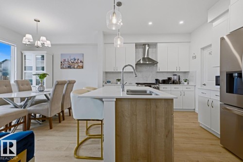Modern kitchen featuring a large central island with wood-finish paneling, an undermount sink, and a chrome faucet - 22924 82 Ave, Edmonton, AB 